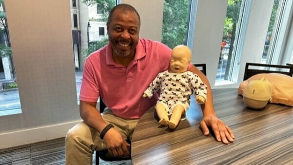Man sits at a table with an infant CPR manikin in an in-person CPR class in Atlanta